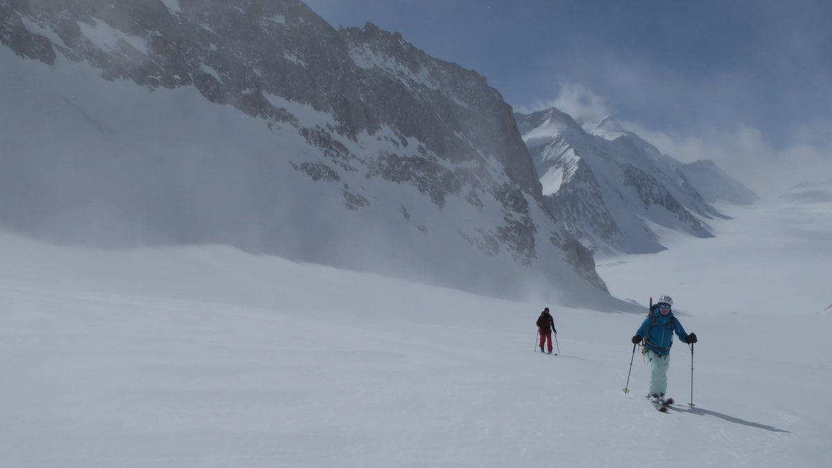 Deux skieurs de randonnée en montée dans la brume au pied de parois