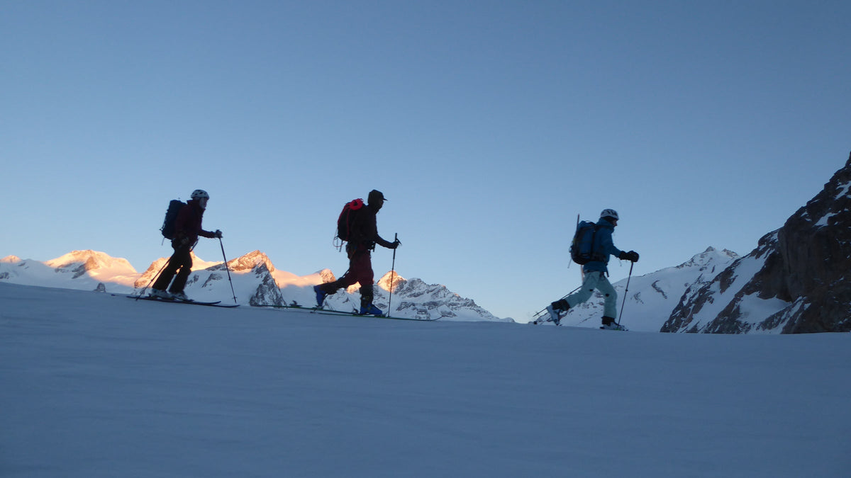 Silhouettes de skieurs de randonnée en montée sur une crête au lever du jour