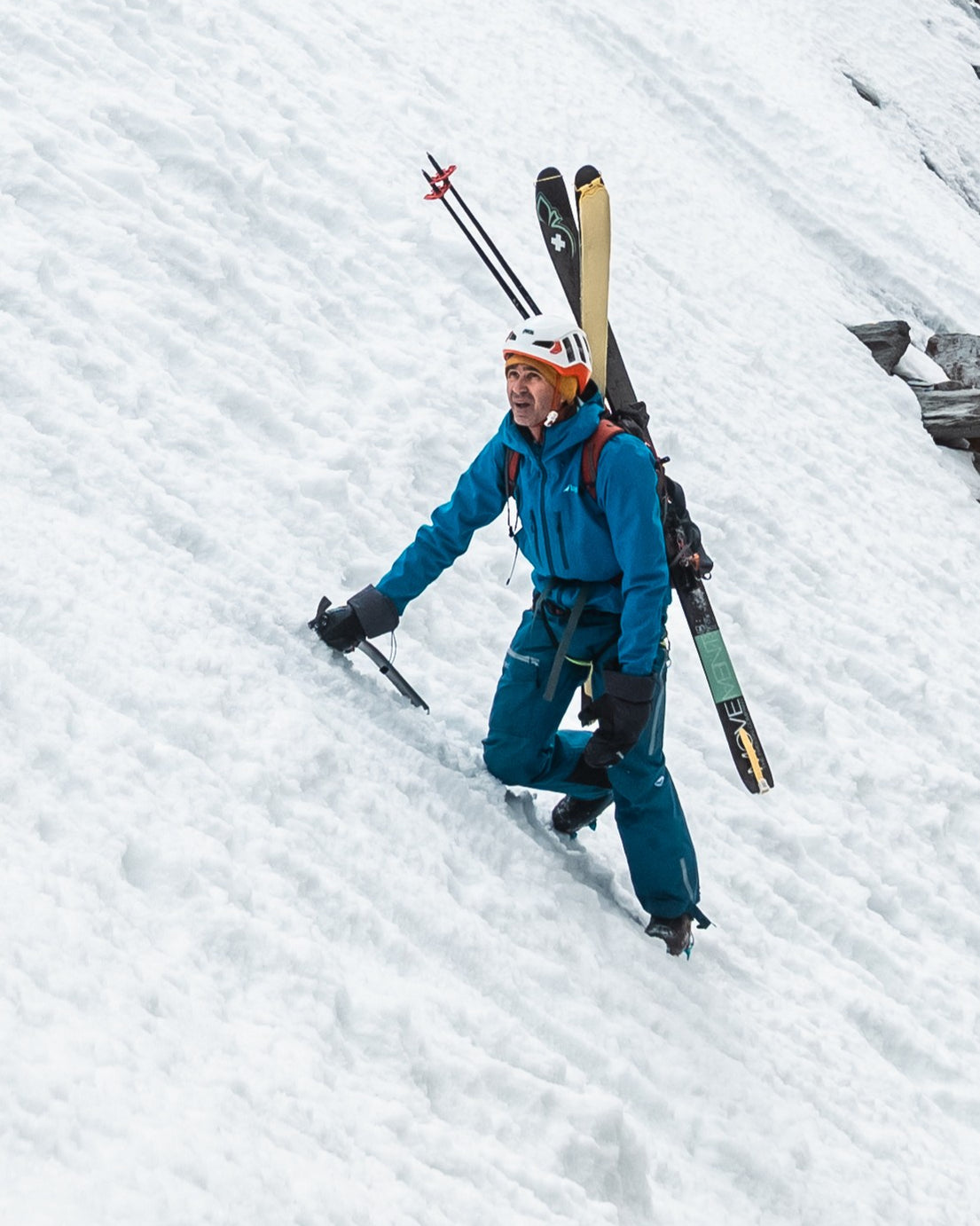 Skieur en montée à pied dans une pente de neige, skis sur le sac