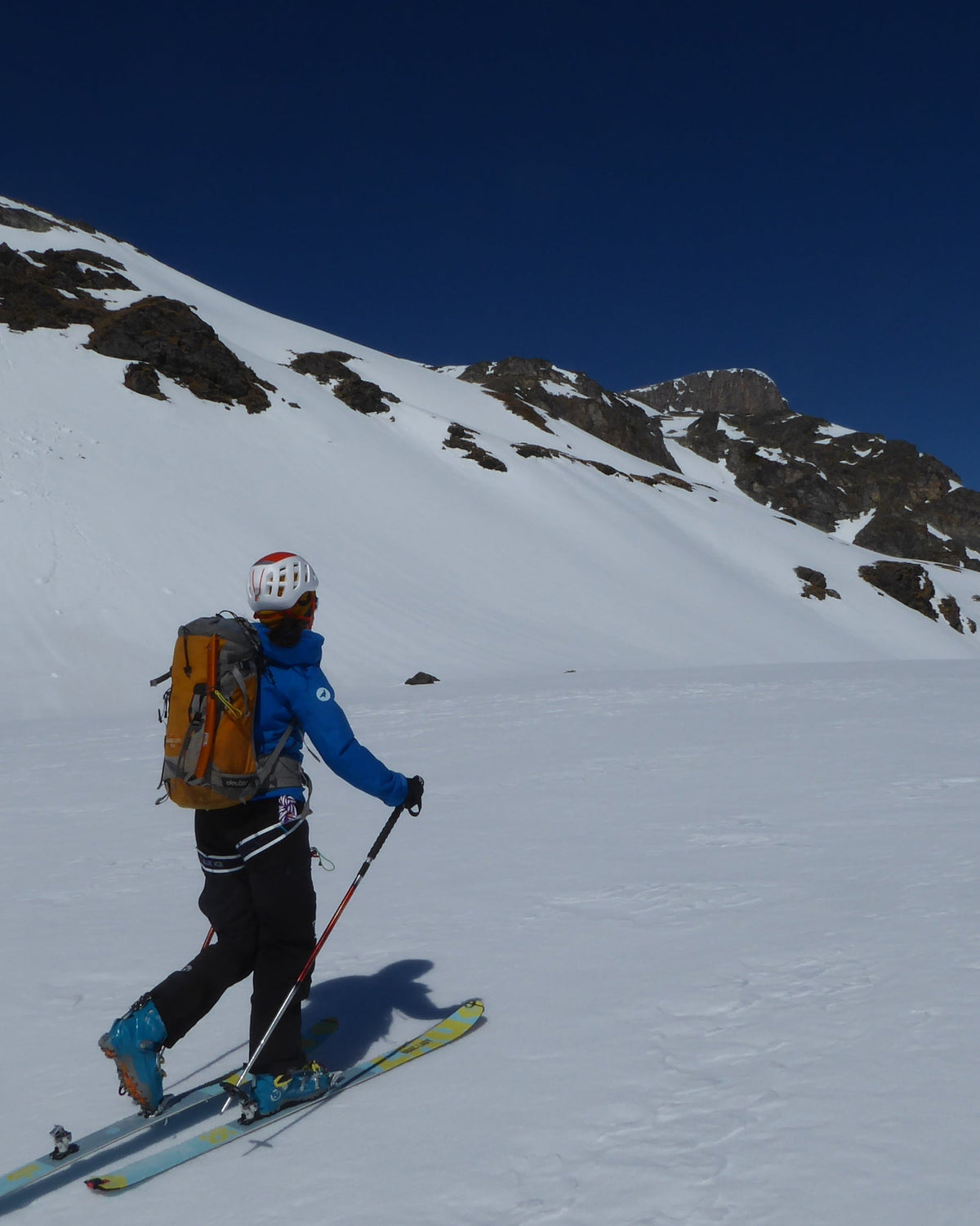Skieur de randonnée en montée sur une pente enneigée ensoleillée