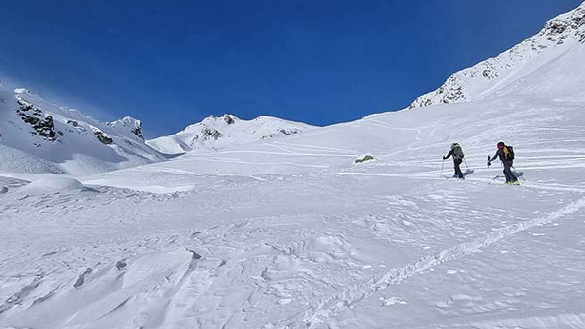 Deux skieurs de randonnée en montée dans un vaste vallon enneigé