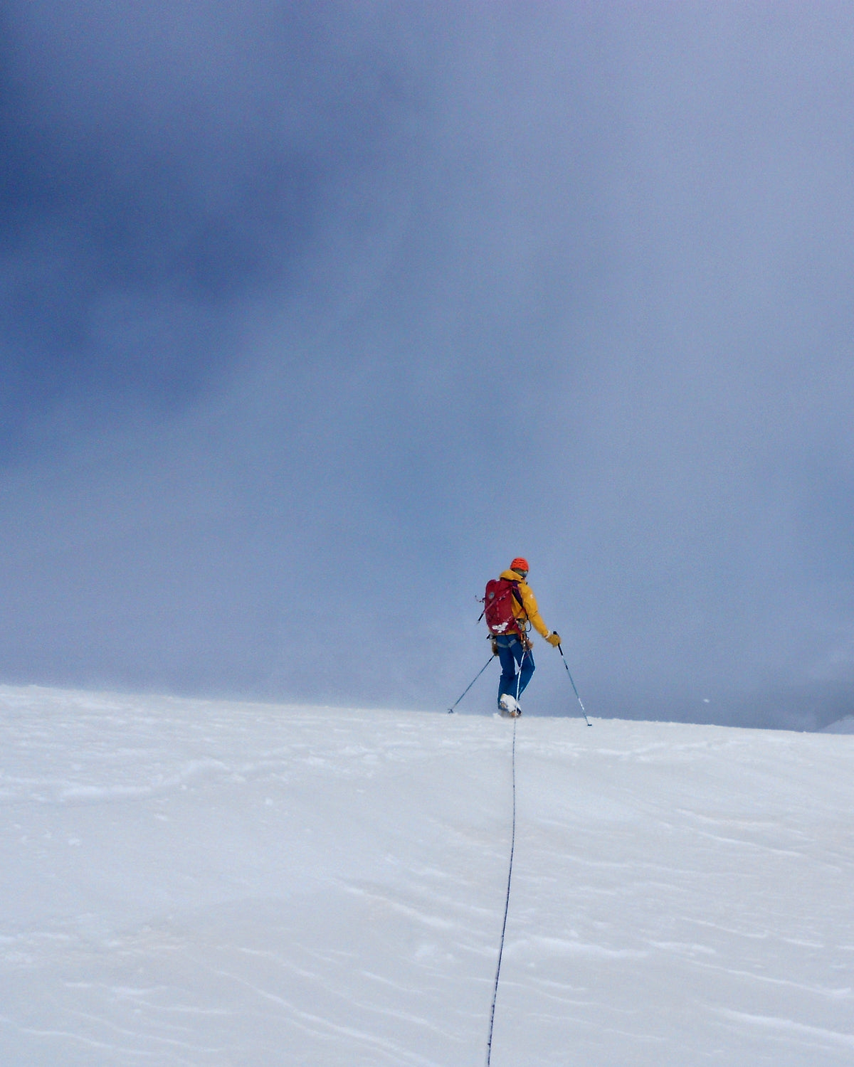 Alpiniste progressant seul sur un vaste glacier enneigé, trace de corde au premier plan