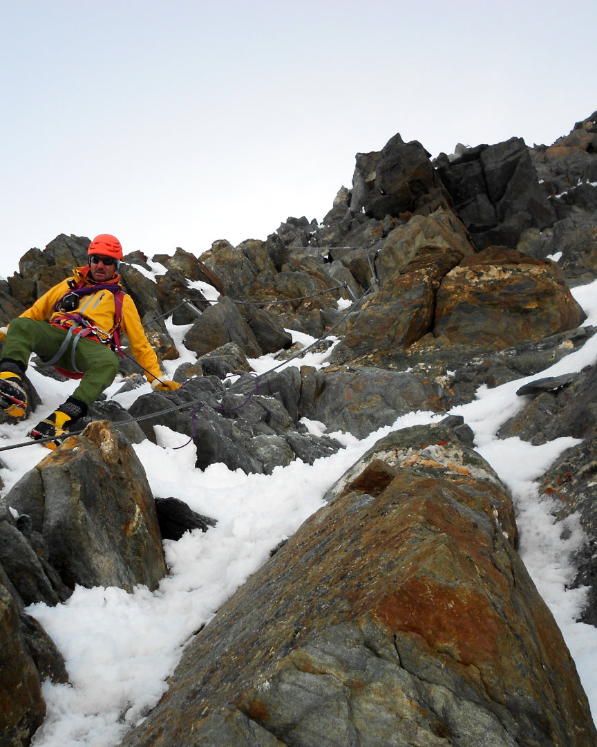 Alpiniste encordé progressant sur une arête rocheuse enneigée, techniques d'évolution en alpinisme