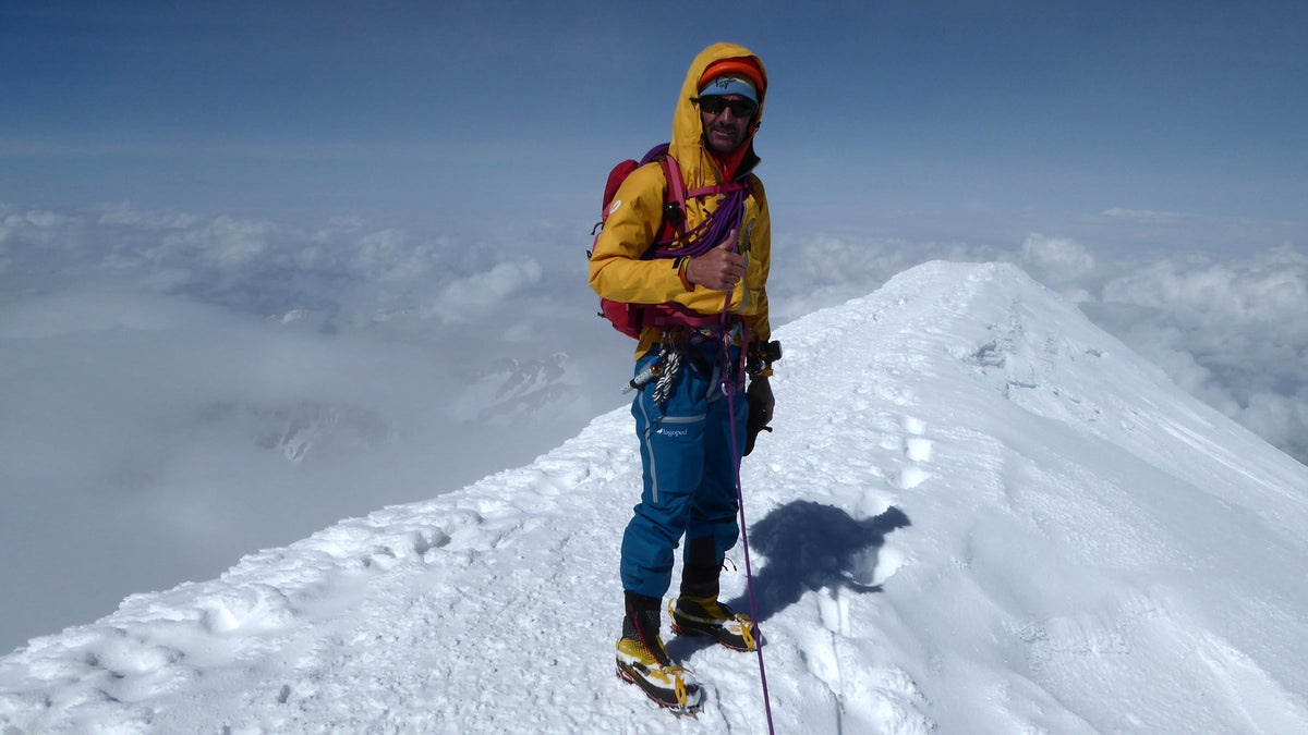 Alpiniste équipé de crampons au sommet d'une arête de neige au-dessus d'une mer de nuages