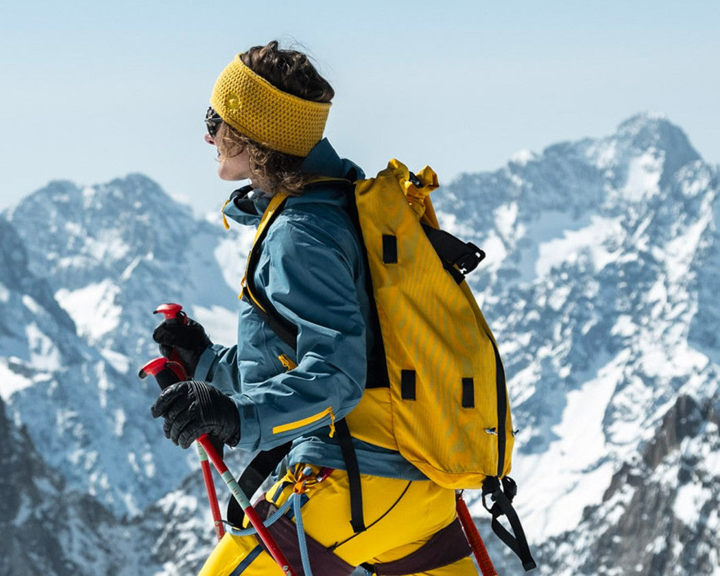 Femme en ski de randonnée, montée en peaux bâtons en main, portant le bandeau Lagoped GHEADBAND soleil face aux sommets enneigés