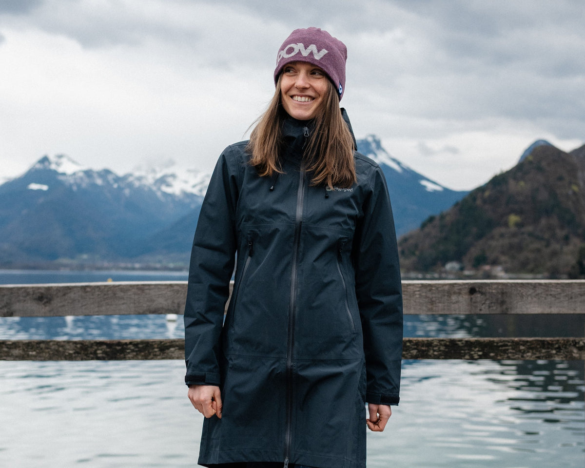 Femme en balade sur un ponton au bord du lac, portant le bonnet en laine Lagoped GEBO POW cassis, montagnes enneigées en arrière-plan