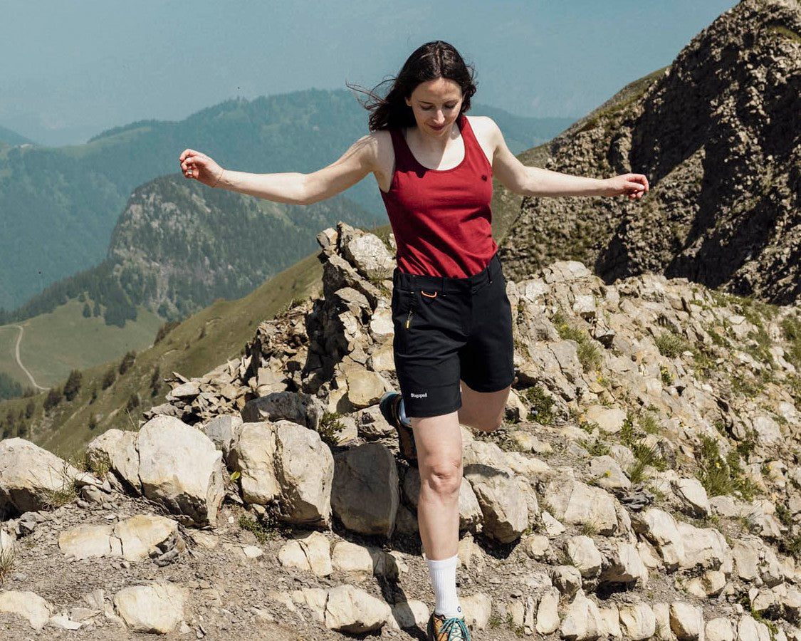 Femme en randonnée descendant une crête rocheuse bras écartés, portant le débardeur Lagoped PRUNELLA granate en montagne