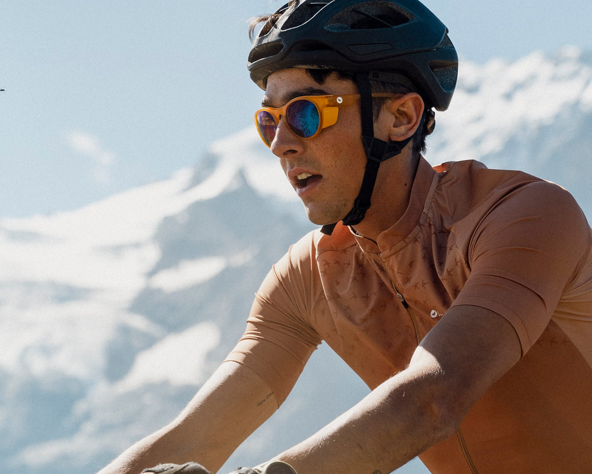 Homme à vélo gravel en plein effort sous les sommets enneigés, portant les lunettes de soleil Lagoped LAGOPEYE CAT3 GreenSoleil