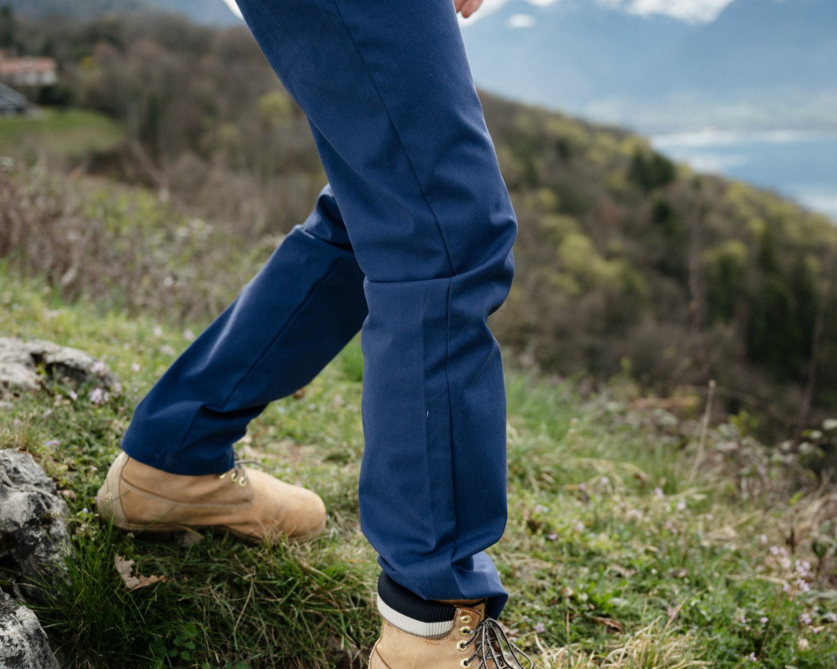 Homme en balade portant le pantalon Lagoped COLCHUUCK navy, pas assuré sur un rocher au-dessus du lac en demi-saison