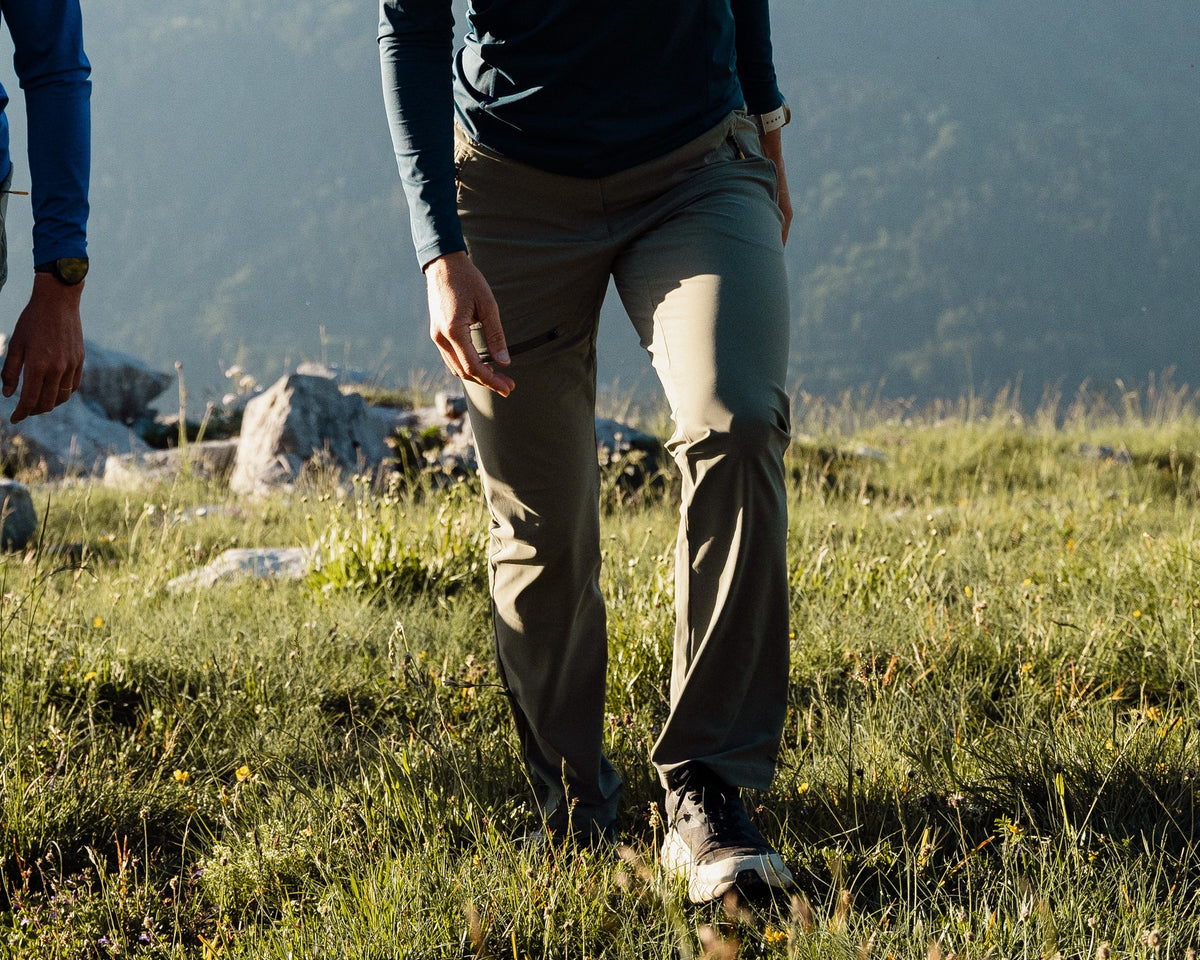 Femme en randonnée portant le pantalon de randonnée Lagoped RIOUPOU vetiver, marche dans l'alpage face aux montagnes