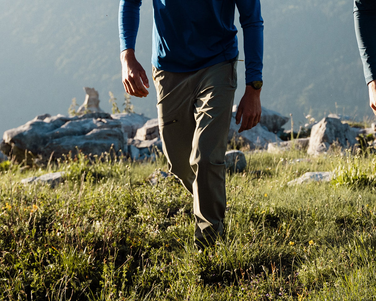 Homme en randonnée portant le pantalon de randonnée Lagoped RIOUPOU vetiver, marche dans l'alpage sous les sommets