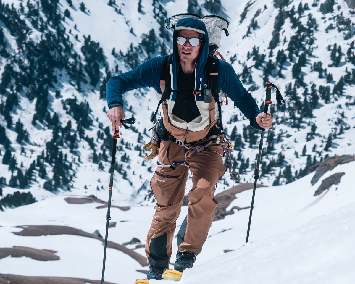 Homme en ski de randonnée portant le pantalon de ski freeride Lagoped SUPARIDE camel, montée en peaux sur un versant enneigé