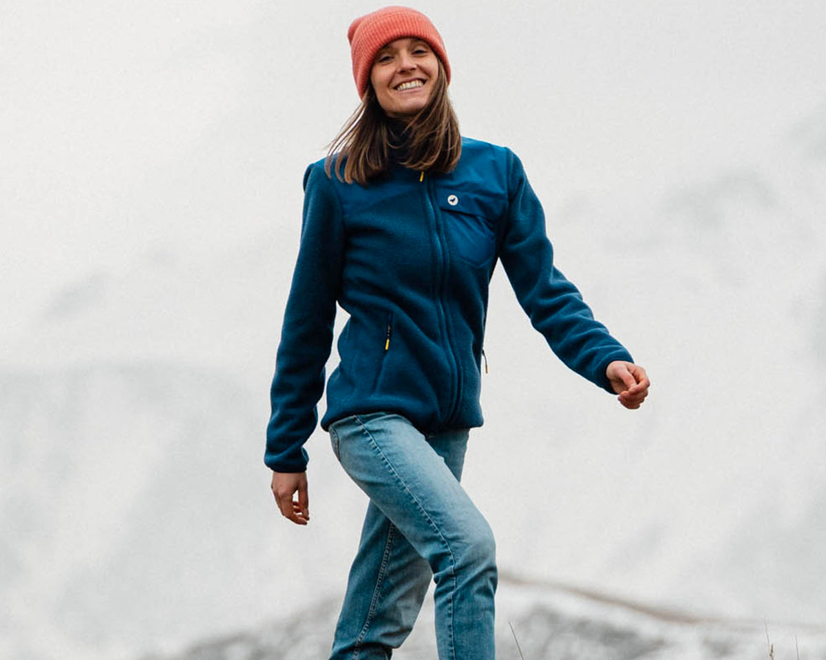 Femme en randonnée portant la polaire Lagoped RYPA navy, descend une crête herbeuse en marchant sous un ciel brumeux d'automne