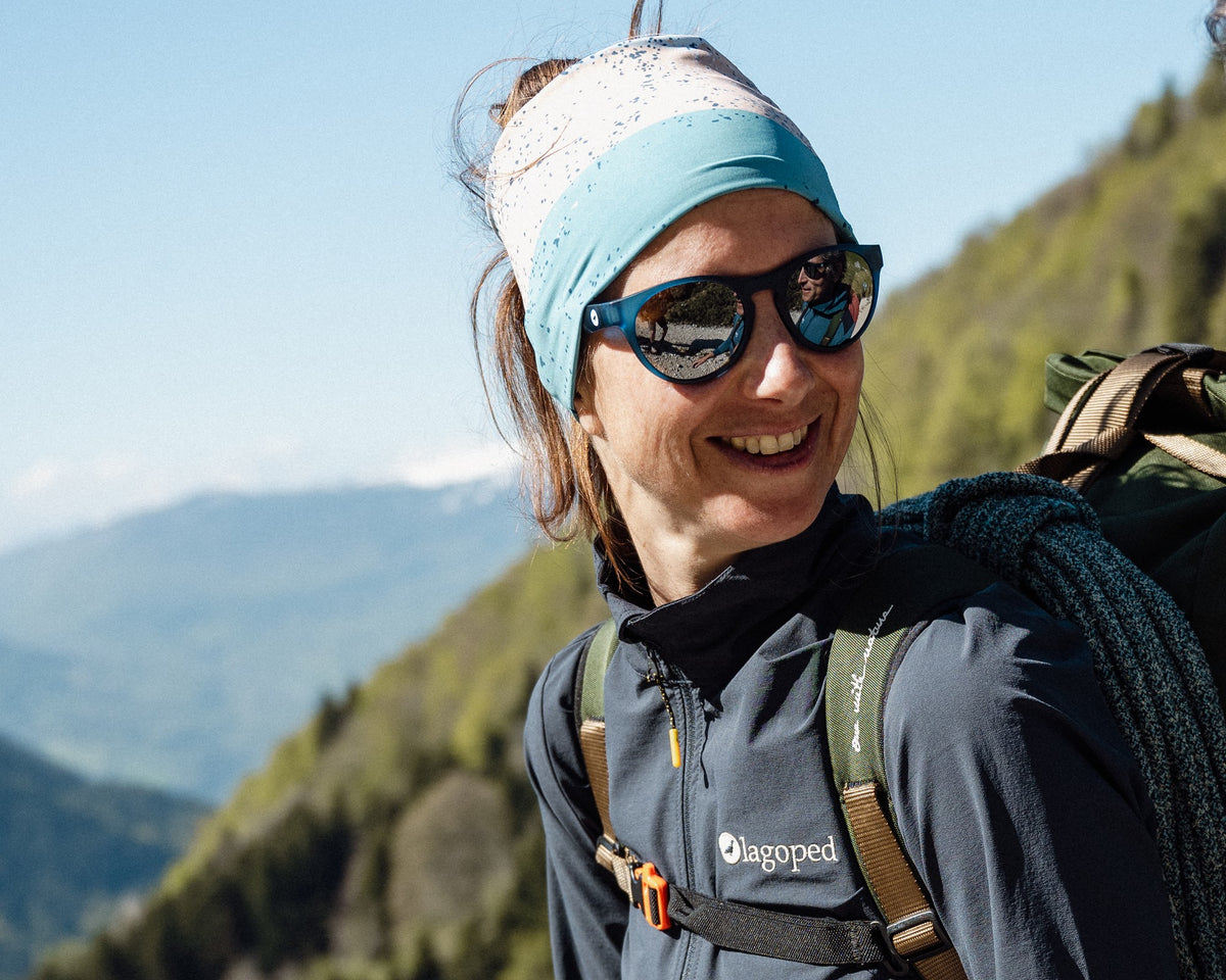 Femme en marche d'approche d'escalade, corde sur le sac, portant le tour de cou Lagoped SUMSNOOD glacier en bandeau, versant boisé