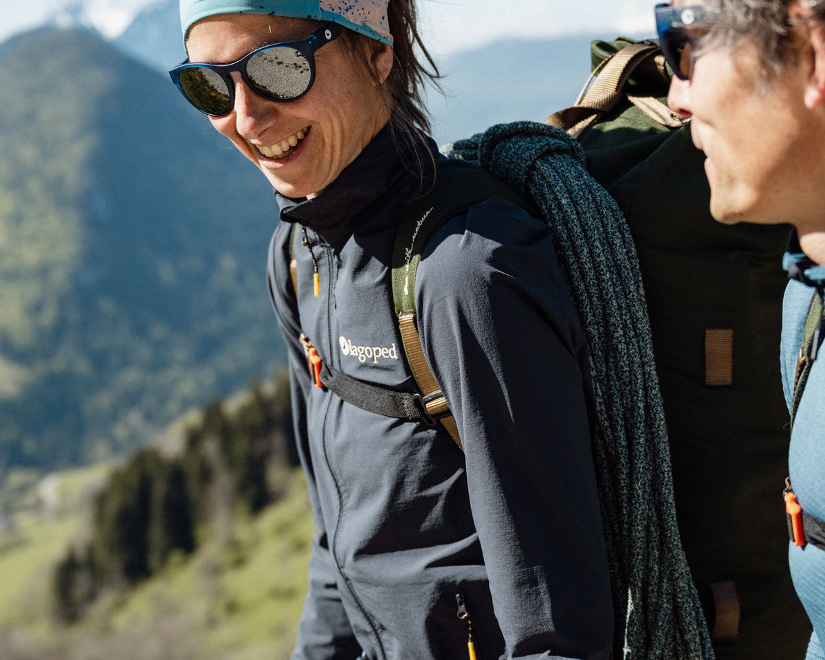 Femme en marche d'approche d'alpinisme, corde sur l'épaule, portant la veste softshell Lagoped UKPIK graphite